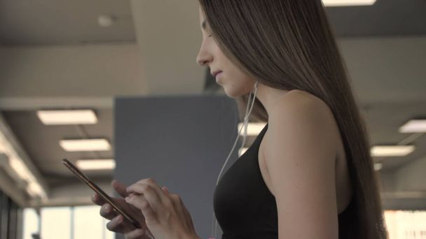 Beautiful sporty girl listen to music from smartphone with app running on treadmill - Φωτογραφία, εικόνα