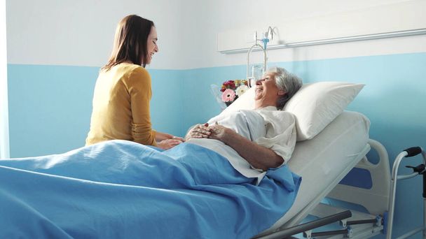 Hastanede büyükannesini ziyaret eden genç bir kadın, mutlular ve birbirlerine bakıyorlar. - Fotoğraf, Görsel