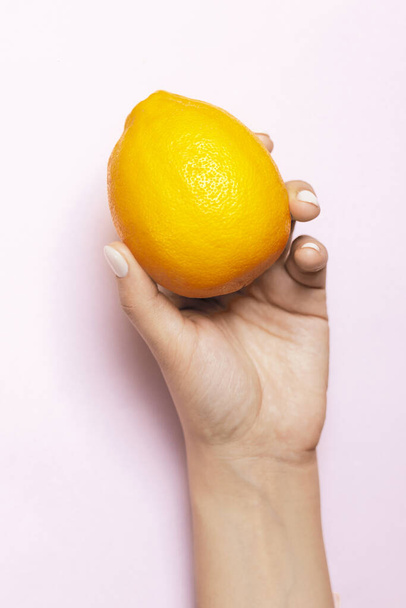 Young woman hand holding a fresh lemon fruit on the bright pink background - Photo, Image