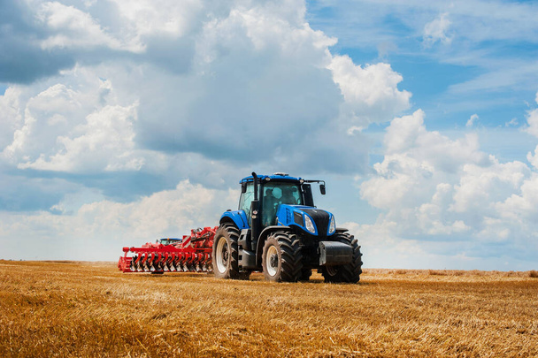 Blauer Traktor, der im Feld arbeitet, Landmaschinen, Feld und schöner Himmel - Foto, Bild