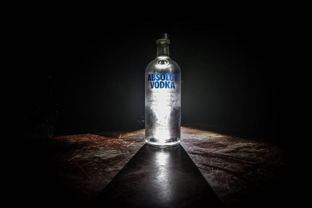 Μπακού, Αζερμπαϊτζάν - Φεβρουάριος 09, 2020: Η Absolut Vodka είναι μια μάρκα βότκας, που παράγεται κοντά στο Ahus, στη Σουηδία. Ανήκει στον γαλλικό όμιλο Pernod Ricard. Μπουκάλι βότκα σε ξύλινο τραπέζι με σκούρο τονισμένο ομιχλώδες φόντο. - Φωτογραφία, εικόνα
