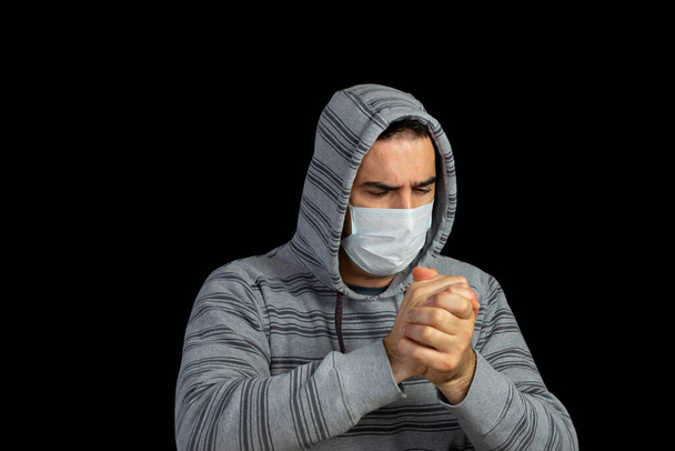 Nuori mies harmaa huppari ja naamio estää sepelvaltimovirus poseeraa musta tausta
 - Valokuva, kuva