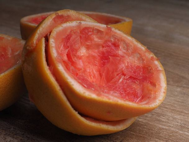 половина вичавленого рожевого грейпфрута на фоні дерева
 - Фото, зображення
