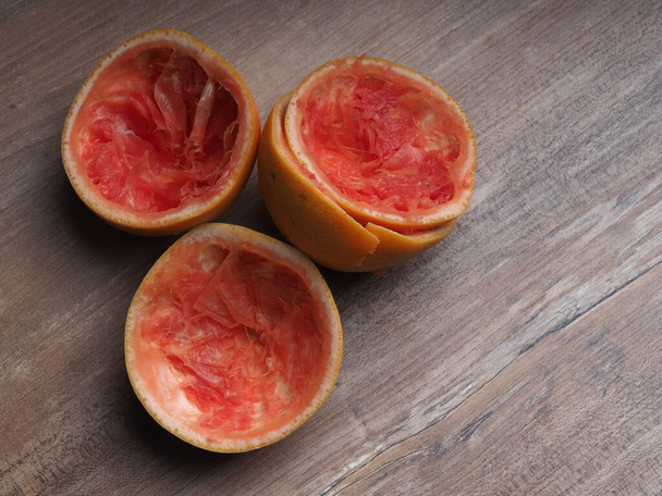 половина вичавленого рожевого грейпфрута на фоні дерева
 - Фото, зображення