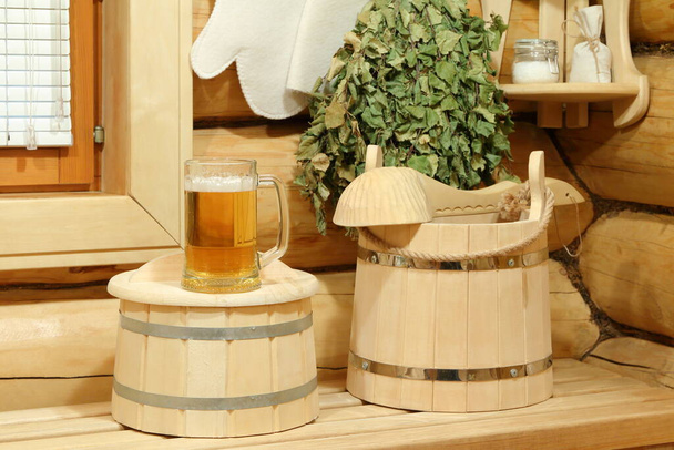 Kubek zimnego piwa lekkiego na drewnianej beczce i akcesoria do sauny.  - Zdjęcie, obraz