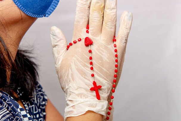 Nő imádkozó fehér sebészeti kesztyű és piros rózsafüzér a kezében Brazíliában. - Fotó, kép