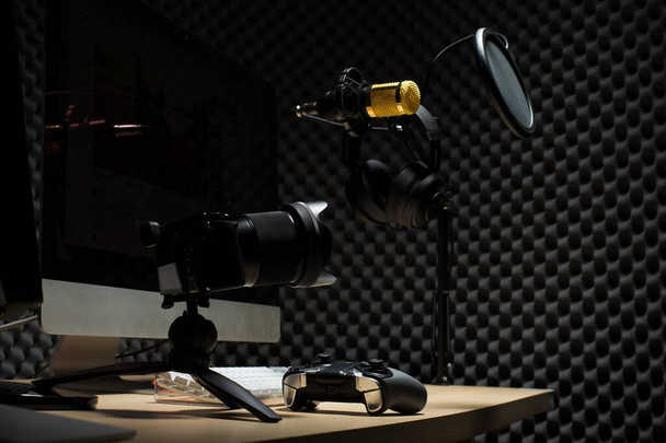 Микрофон конденсатор, золотой микрофон висит над звукопоглощающей стеной комната с волновым монитором клавиатуры клавиатуры контроллер мыши и наушники в темной студии аудио, низкая экспозиция освещения фоновое пространство копирования
 - Фото, изображение