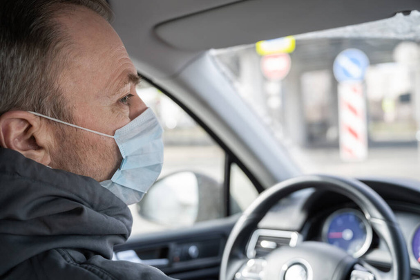 Kendini araba kullanan bakteri ve virüsten korumak için maske takan orta yaşlı bir adamın yüzü. Coronavirus. Salgın - Fotoğraf, Görsel