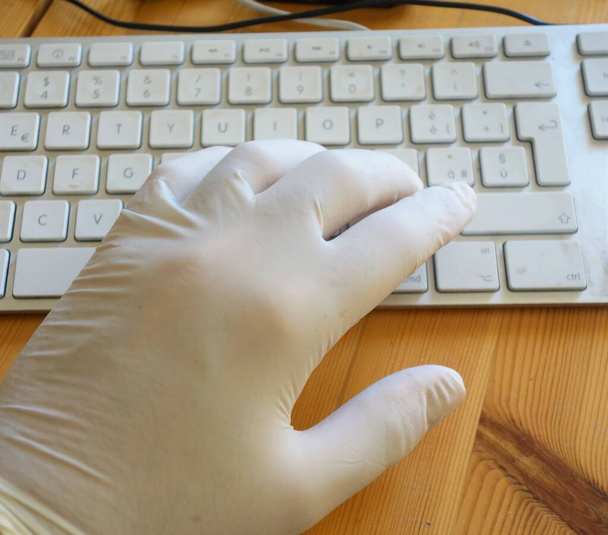 Smart working in order to prevent the spread of respiratory diseases like coronavirus COVID-19. Hand wearing a latex glove typing on a computer keyboard - Photo, Image