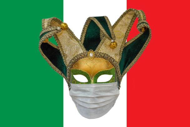 Klassiek Venetiaans carnavalsmasker in een medisch beschermend masker tegen de achtergrond van de vlag van Italië. Het concept van de verspreiding van het coronavirus in Italië - Foto, afbeelding