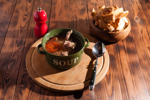 Sopa de osso de carne rústica / caldo polvilhado com cebolas verdes em uma mesa de madeira com biscoitos finos
. - Foto, Imagem