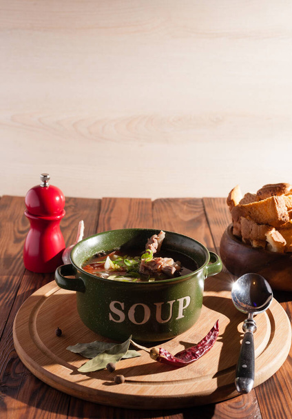 Sopa de osso de carne rústica / caldo polvilhado com cebolas verdes em uma mesa de madeira com biscoitos finos
. - Foto, Imagem