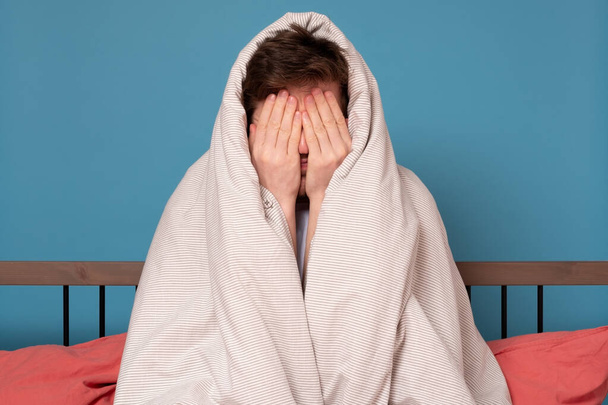 Vystrašený mladík zakrývající obličej ve stresu, jak sedí v posteli. Koncepce karantény nebo izolace. - Fotografie, Obrázek