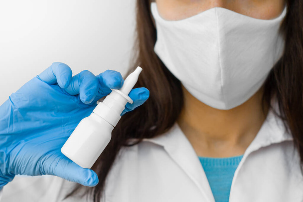 Žena, která používá nosní sprej k léčbě chřipky nebo tekoucí nos, drží lék v ruce. Lékař v ochranné masce a modré rukavice ukazuje nos sprej pro léčbu nemoci - Fotografie, Obrázek