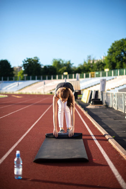Athlète fille tord son tapis après avoir fait du sport sur une journée d'été ensoleillée au stade
 - Photo, image