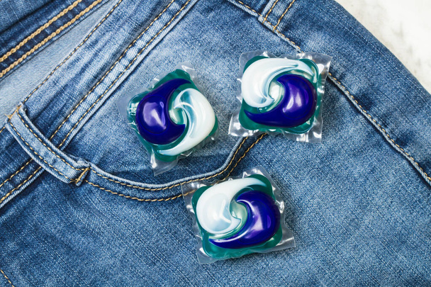 Tre cialde detergenti per lavatrice su un blue jeans in vista dall'alto
 - Foto, immagini