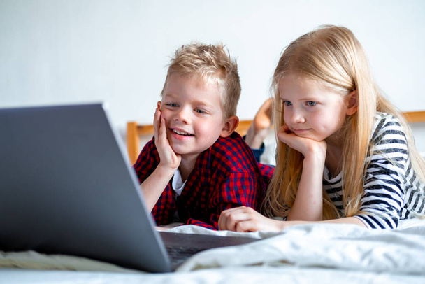 Distance learning online education. Schoolboy and girl studying at home with digital tablet laptop notebook and doing school homework. Sitting on bed with training books. - Fotografie, Obrázek