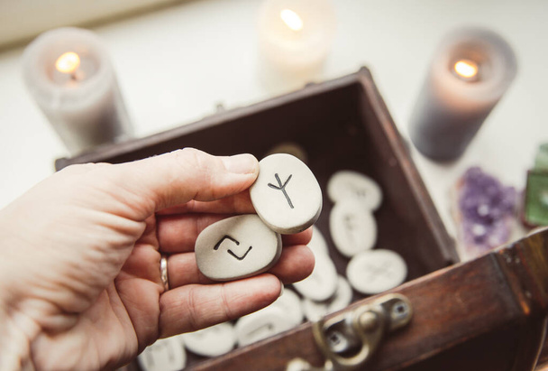 Hand holding rune stones, taking out of the wooden box container, self-prophecy concept. Candles burning, copy space. - Photo, Image