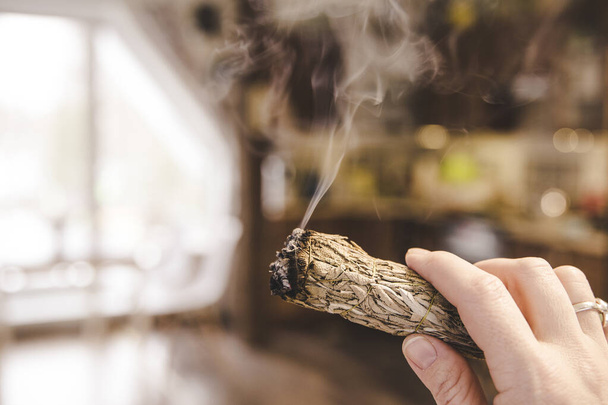 Mulher mão segurando pacote de ervas de pó de sálvia seco vara fumando. Acredita-se para limpar a energia negativa e purificar espaços de estar em casa em quartos
. - Foto, Imagem