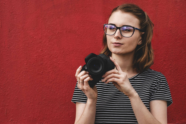 Reflexiva joven fotógrafa observadora sobre una pared roja
  - Foto, imagen