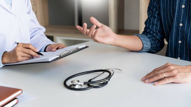 doctor working with patient taking notes with clipboard and discussing something in his medical office, health care and people concept - Photo, Image