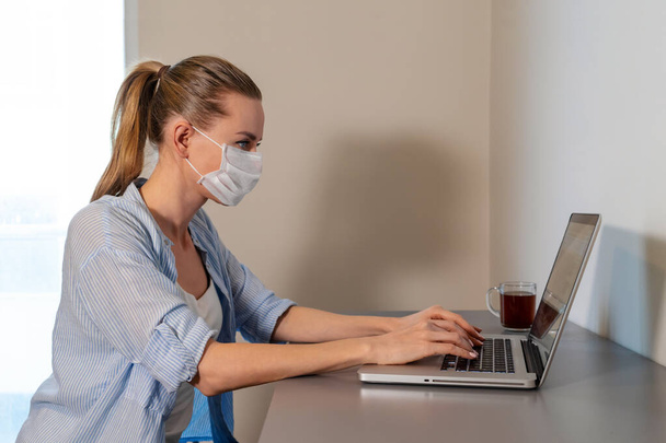 online education and home office work. woman with medical mask working remotely from home Using computer. Self isolation. Quarantine. pandemic, coronavirus, corona, covid-19 - Foto, afbeelding
