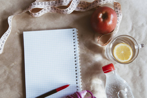 Σχεδιασμός δίαιτας. Προτίμηση γεύματος - υγιεινή διατροφή: Μπουκάλι γλυκού νερού, σχοινάκι και ένα μήλο με άδειο σημειωματάριο - Φωτογραφία, εικόνα