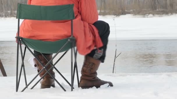 Un pêcheur s'assoit sur un tabouret en hiver et attrape un poisson. Une rivière qui coule en arrière-plan. Le rivage est couvert de neige
 - Séquence, vidéo