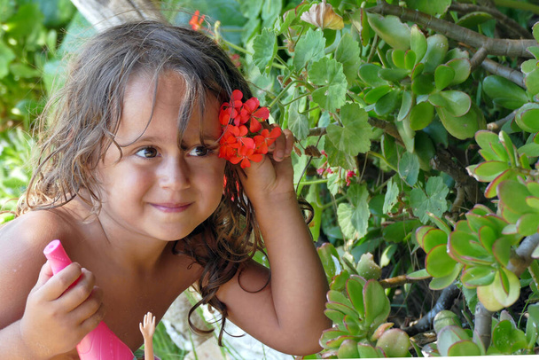 una hermosa niña de 4 años y medio usa un geranio rojo para decorar su cabello - Foto, imagen