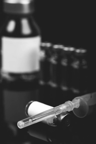 Viales médicos inyectables con jeringa y ampollas sobre fondo negro. Foto en blanco y negro
. - Foto, imagen