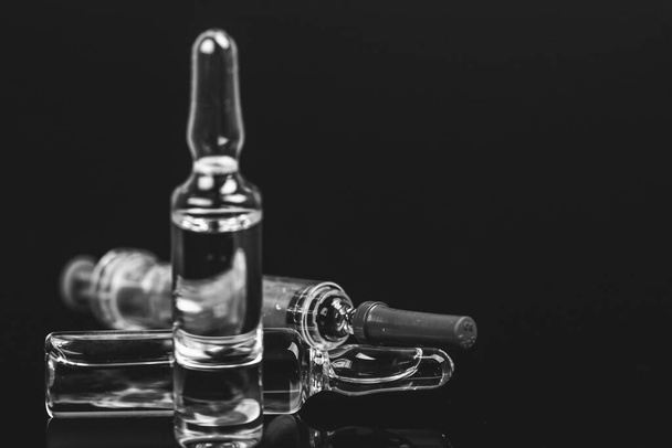 Sterile medical vials with medication solution, ampoules, and syringe isolated on a black background. Black and white photo. - Foto, imagen