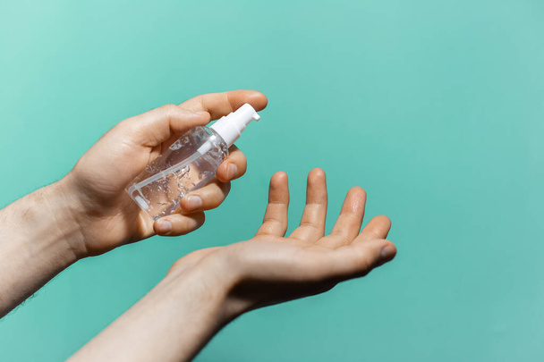 Close-up van de mannelijke handen van toepassing ontsmettingsmiddel antiseptische gel op de achtergrond van aqua menthe kleur. Man met behulp van fles antibacteriële zeep. - Foto, afbeelding