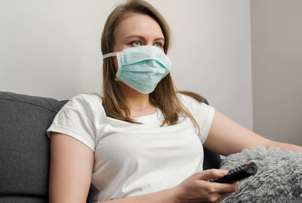 Woman in medical mask watching TV. Quarantine at home. - Fotó, kép