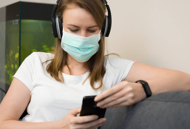 Жінка в медичній масці слухає музику. Ізоляція в домашніх умовах
. - Фото, зображення