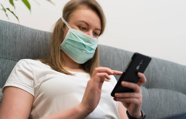 Femme en masque médical utilisant un téléphone portable. Isolement à la maison. - Photo, image