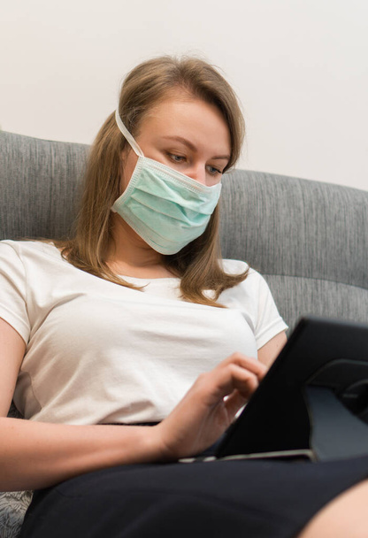 Mujer con máscara médica usando tableta pc. Aislamiento en casa
. - Foto, imagen