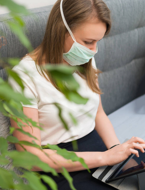 Γυναίκα με ιατρική μάσκα χρησιμοποιώντας το tablet pc. Απομόνωση στο σπίτι. - Φωτογραφία, εικόνα