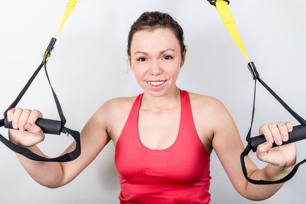 Upper body exercise concept. Image of beautiful woman exercising with suspension straps alone in studio. TRX concept isolated on white background. - Photo, Image