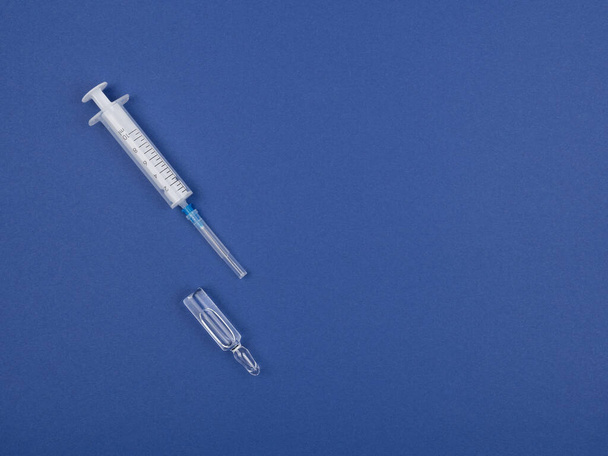 Jeringa con aguja y ampolla sobre fondo azul. La vista desde arriba
. - Foto, imagen