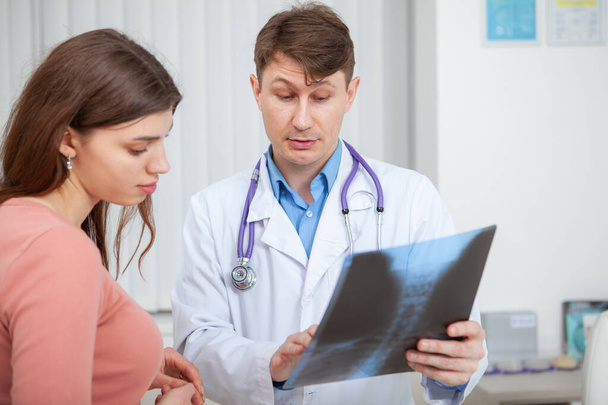 Rijpere arts onderzoekt röntgenscan van zijn vrouwelijke patiënt tijdens medische afspraak - Foto, afbeelding
