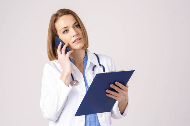 Portrait shot of middle aged female doctor having a call while standing at isolated background. - Photo, image