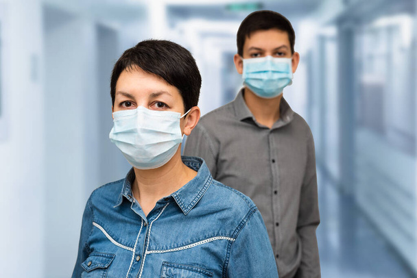 Két ember védőmaszkot visel a kórházban vagy az orvosi központban. Kaukázusi középkorú nő és tinédzser fiú orvosi maszkban. COVID-19 járványmegelőzés. Coronavirus pandémiás fogalom - Fotó, kép