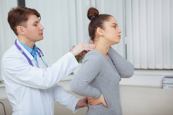 Mulher jovem que sofre de dor nas costas médico visitante no hospital. Quiroprático examinando dor nas costas de uma paciente do sexo feminino
 - Foto, Imagem