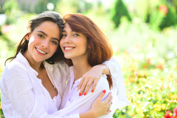 Best friends. Happy women friends standing in park. looking at camera. Young women in white shirt are walking on the green field. - 写真・画像