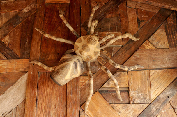 Grande tarantola sulla parete di tavole piallate grezze. Statua Enorme ragno in legno. Ragno giocattolo marrone sul pavimento di legno. Focus selettivo
. - Foto, immagini