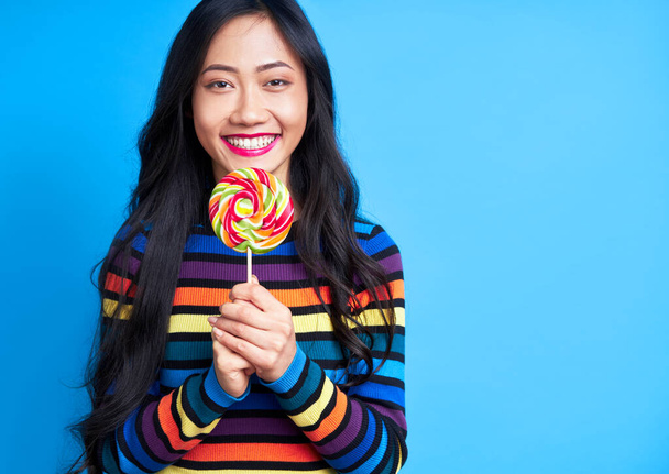 Happy beautiful woman with colorful lollipop isolated on blue background. Sweet food, enjoying concept                               - Foto, imagen
