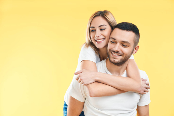Happy smiling couple in love on yellow background with copy space. Man carrying his girlfriend piggyback. Love, romance, fun concept                            - Φωτογραφία, εικόνα