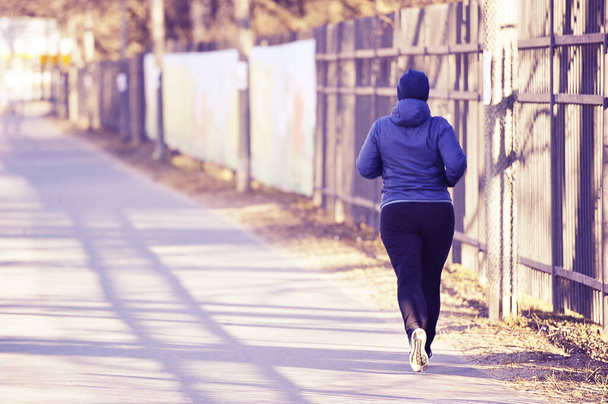's morgens joggen in het park - een vrouw in een sportuniform loopt langs de stoep - Foto, afbeelding