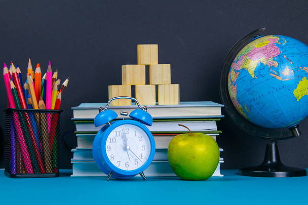 Una pila de libros con un globo, un vaso de lápices, un reloj y manzanas
. - Foto, Imagen