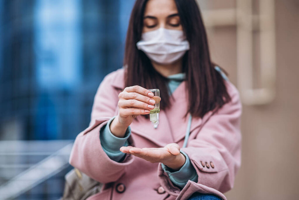 Close up hands of female in medical mask cleaning her hands with sanitizer outdoor in the city to prevent virus deseases. Coronavirus, COVID-19, epidemic, pandemic, quarantine concept - Foto, Imagen